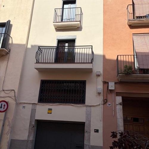 Fachada entre medianeras con balcón de forja y acceso a garaje